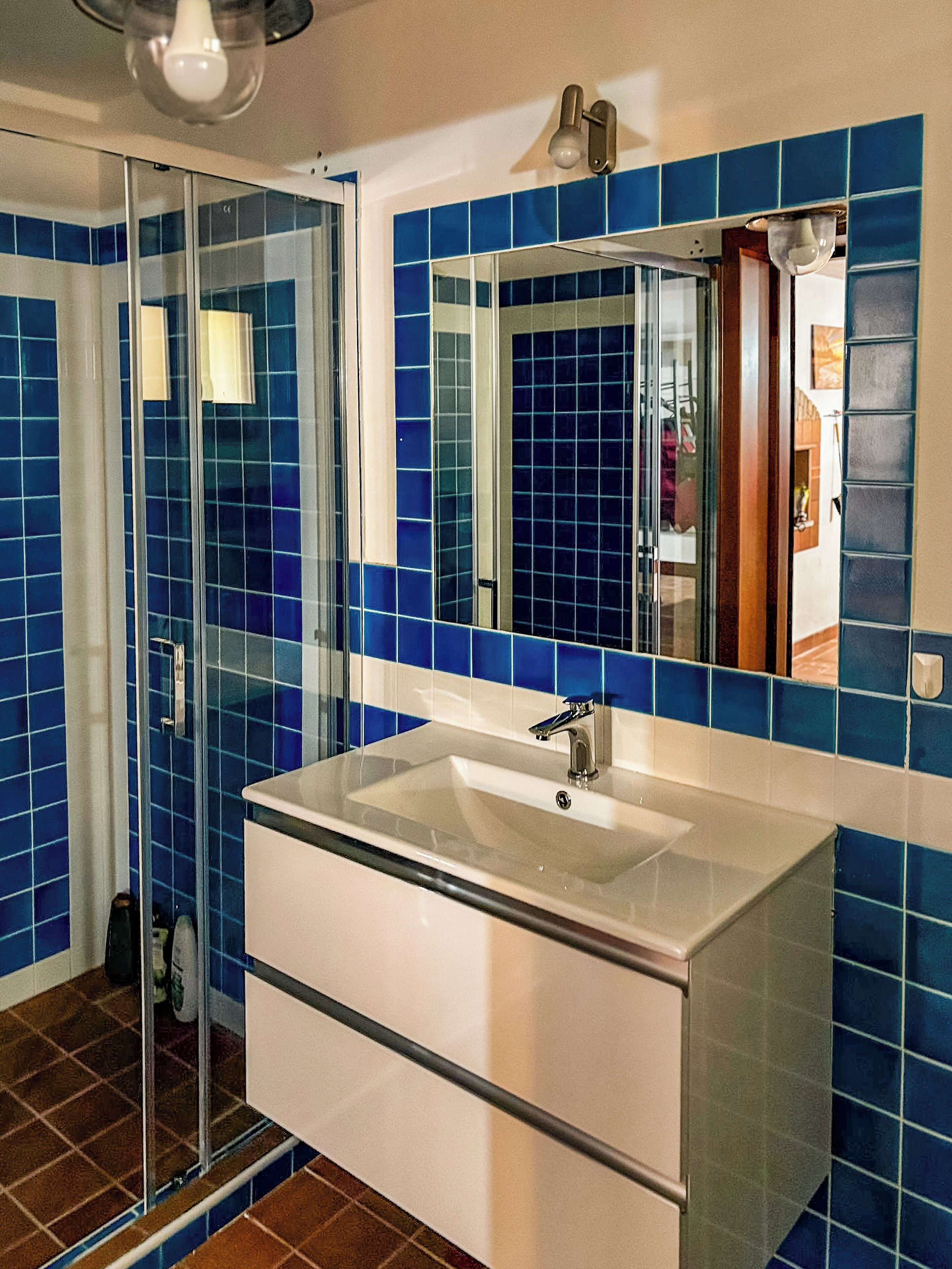 A bathroom with a glass shower enclosure, a white sink with a single faucet, and blue-tiled walls.
