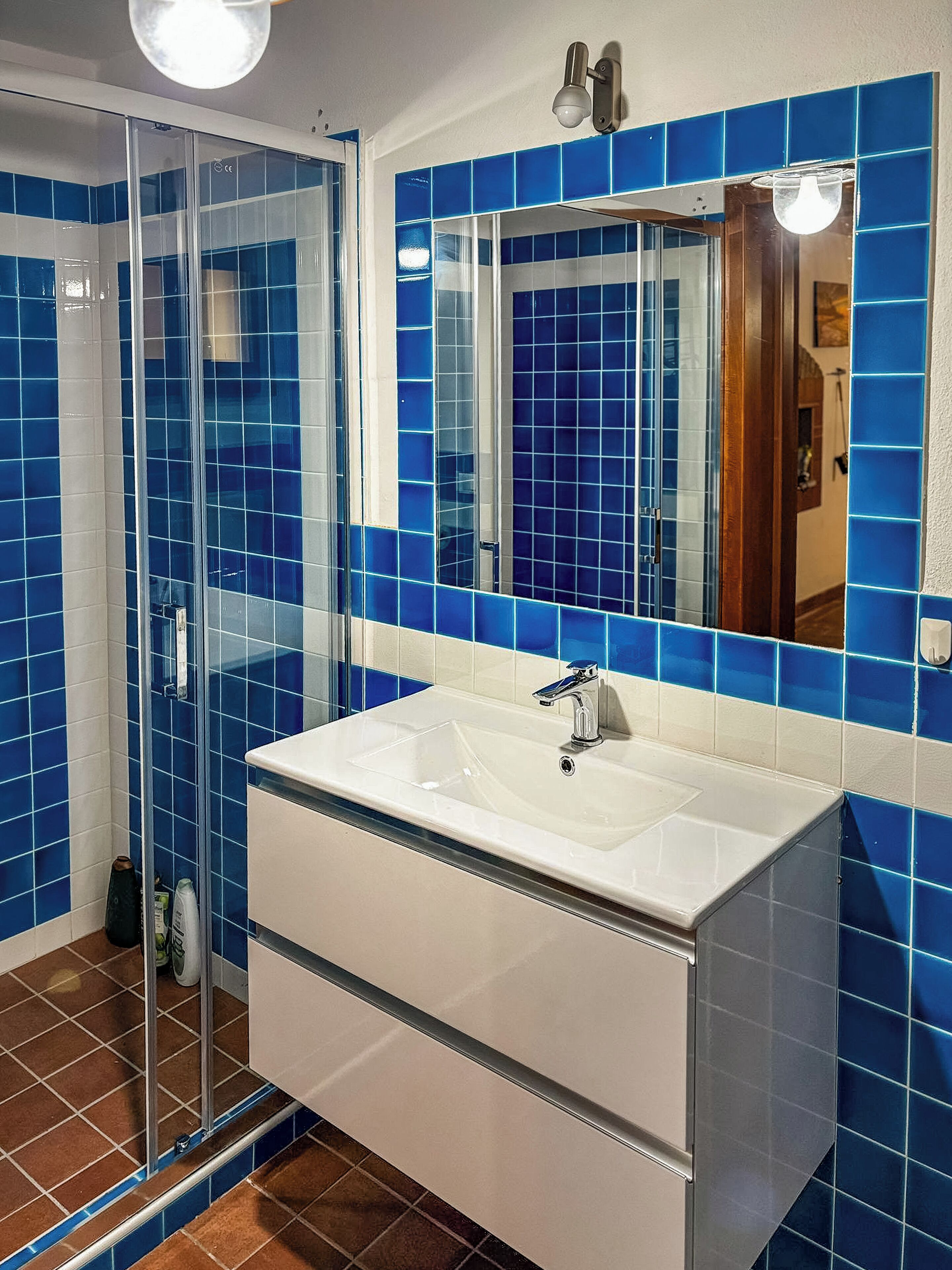 Un baño con cabina de ducha de vidrio, lavabo blanco y paredes con azulejos azules.