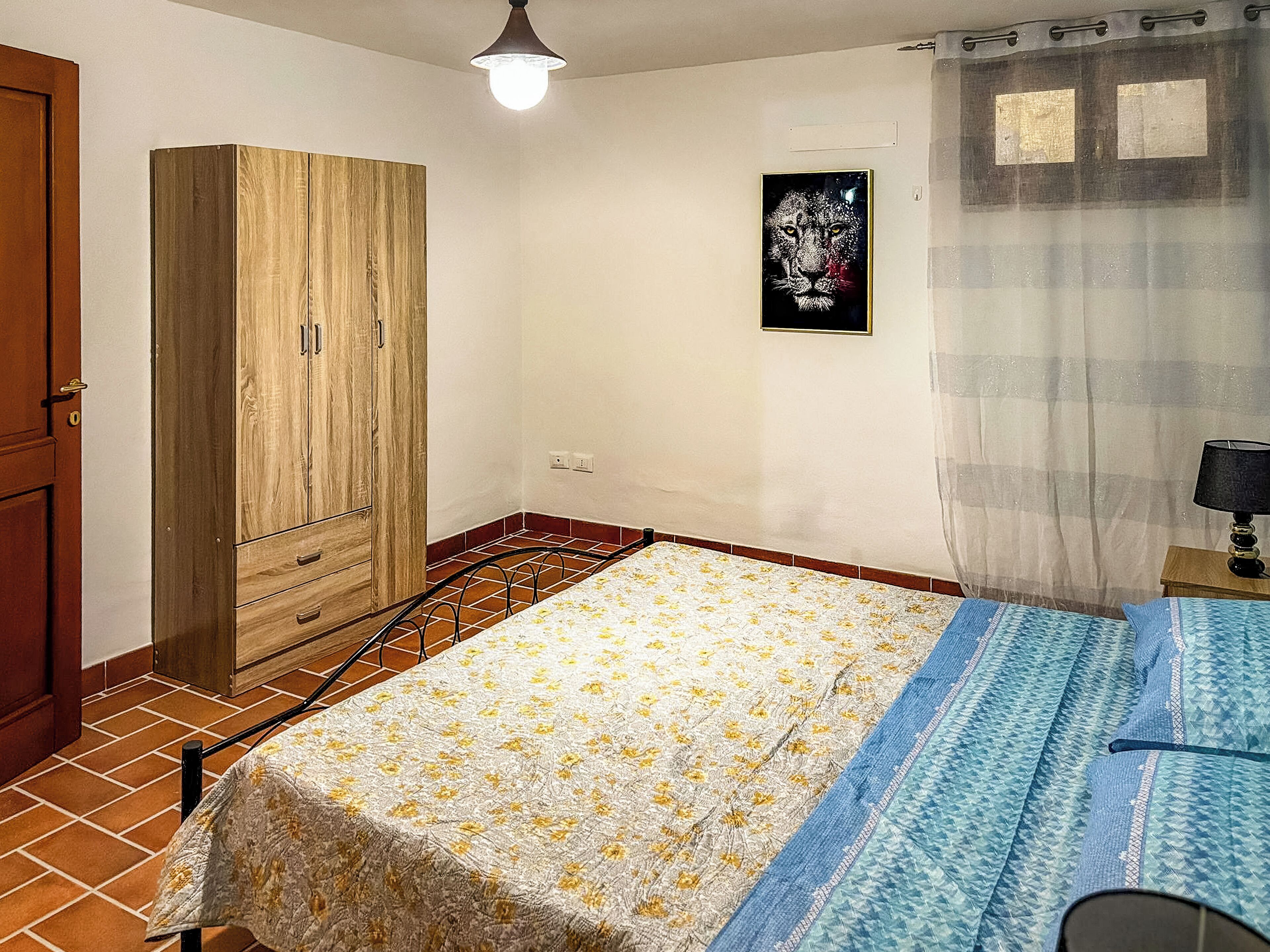 A bedroom with a bed, a wardrobe, a painting, a lamp, and a curtain.