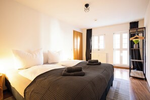Hotellihuone, jossa on suuri sänky, vaatekaappi, ikkuna ja amppelissa roikkuva kasvi.