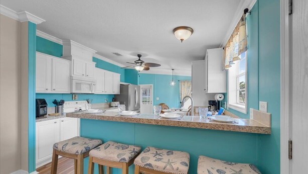 A kitchen with white cabinets, a central island with stools, a ceiling fan, and a window with curtains. - Fish, Boat & Relax-Direct Access Canal Home Near Top Fishing Spots (Punta Gorda)