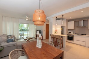 A modern living room with a wooden dining table, a sofa, and a kitchen area with white cabinets and a microwave. - Pool View and 2 min from the beach: Condo in El Cortecito (Punta Cana)