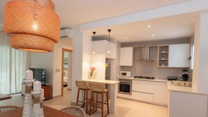 Una cucina moderna con mobili bianchi, un'isola centrale, sgabelli da bar e un lampadario arancione.