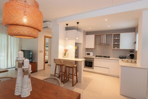 A modern kitchen with white cabinets, a central island, bar stools, and a hanging orange light fixture. - Pool View and 2 min from the beach: Condo in El Cortecito (Punta Cana)