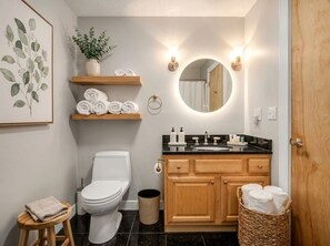 Un bagno con il water, lavandino, mobiletto in legno, porta asciugamani e uno specchio con illuminazione.