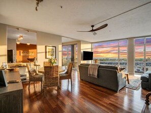 A spacious living area with a large window, a ceiling fan, and a dining area with wicker furniture. - Lakeview Condo + Balcony + Parking + Gym (Cleveland)