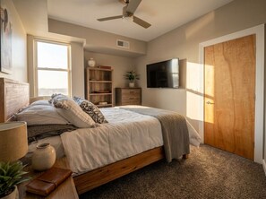 Una camera da letto con un letto, una ventola a soffitto, una TV, una porta in legno e una finestra.