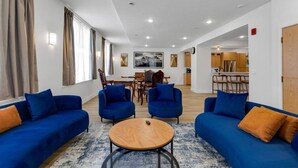 Un salon moderne avec des canapés bleus, une table basse ronde en bois et un coin repas avec des chaises en bois.