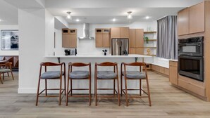 Une cuisine moderne dotée d’un îlot central, de meubles en bois, d’appareils électroménagers en acier inoxydable et de tabourets de bar.