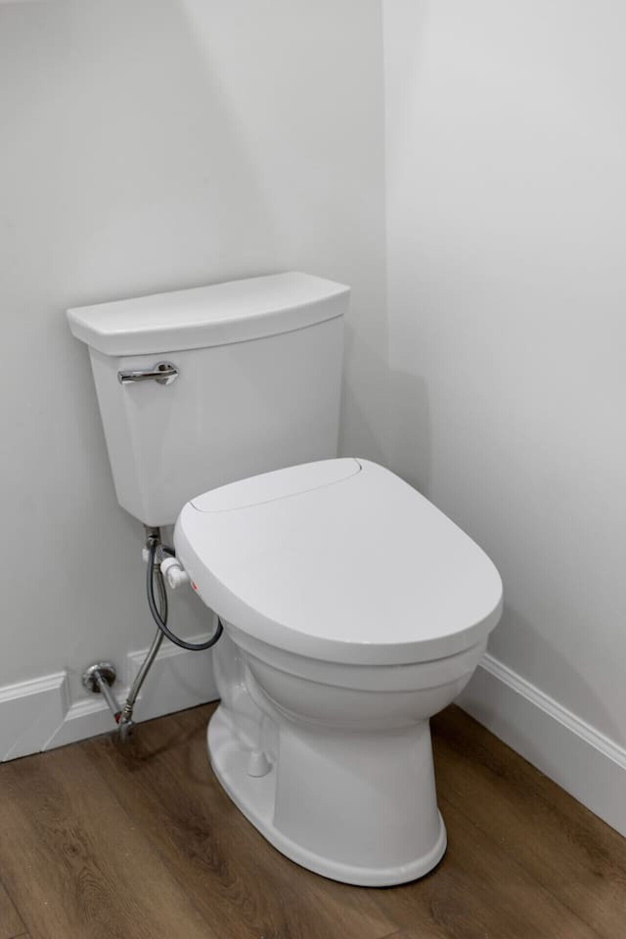 A white toilet with a tank and seat, connected to a wall-mounted flush handle.