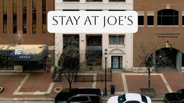 Un immeuble hôtelier à plusieurs étages, de style architectural classique, avec une entrée centrale surmontée d’un auvent et une enseigne indiquant le nom de l’hôtel : « Joe’s ».