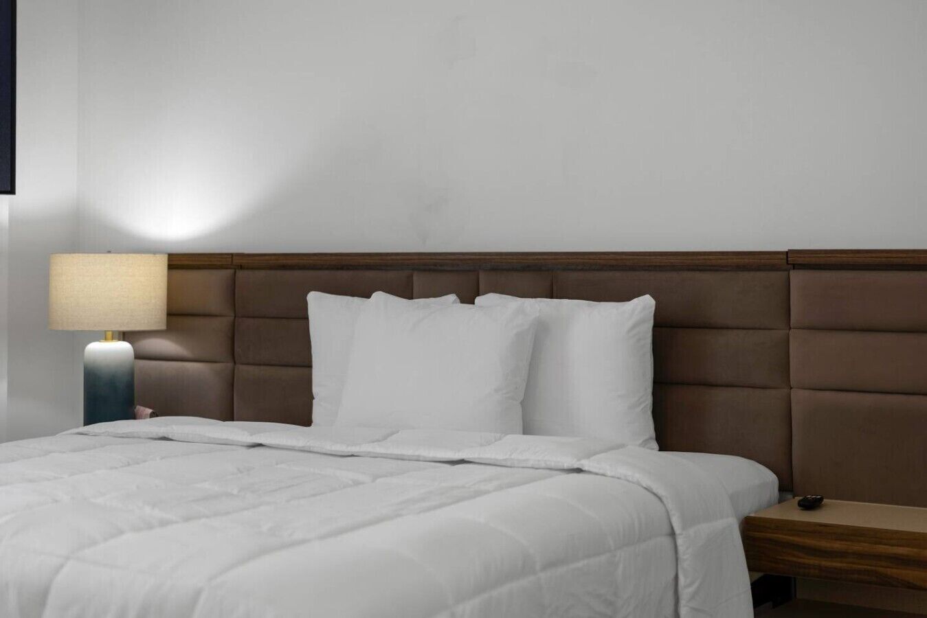 Un lit bien fait, avec une literie blanche, une tête de lit en bois et une lampe de chevet.