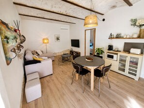 A cozy living area with a sofa, a dining table with chairs, a TV, and a kitchen area with a microwave. - Stone farmhouse near Grignan château in Drôme (Roynac)