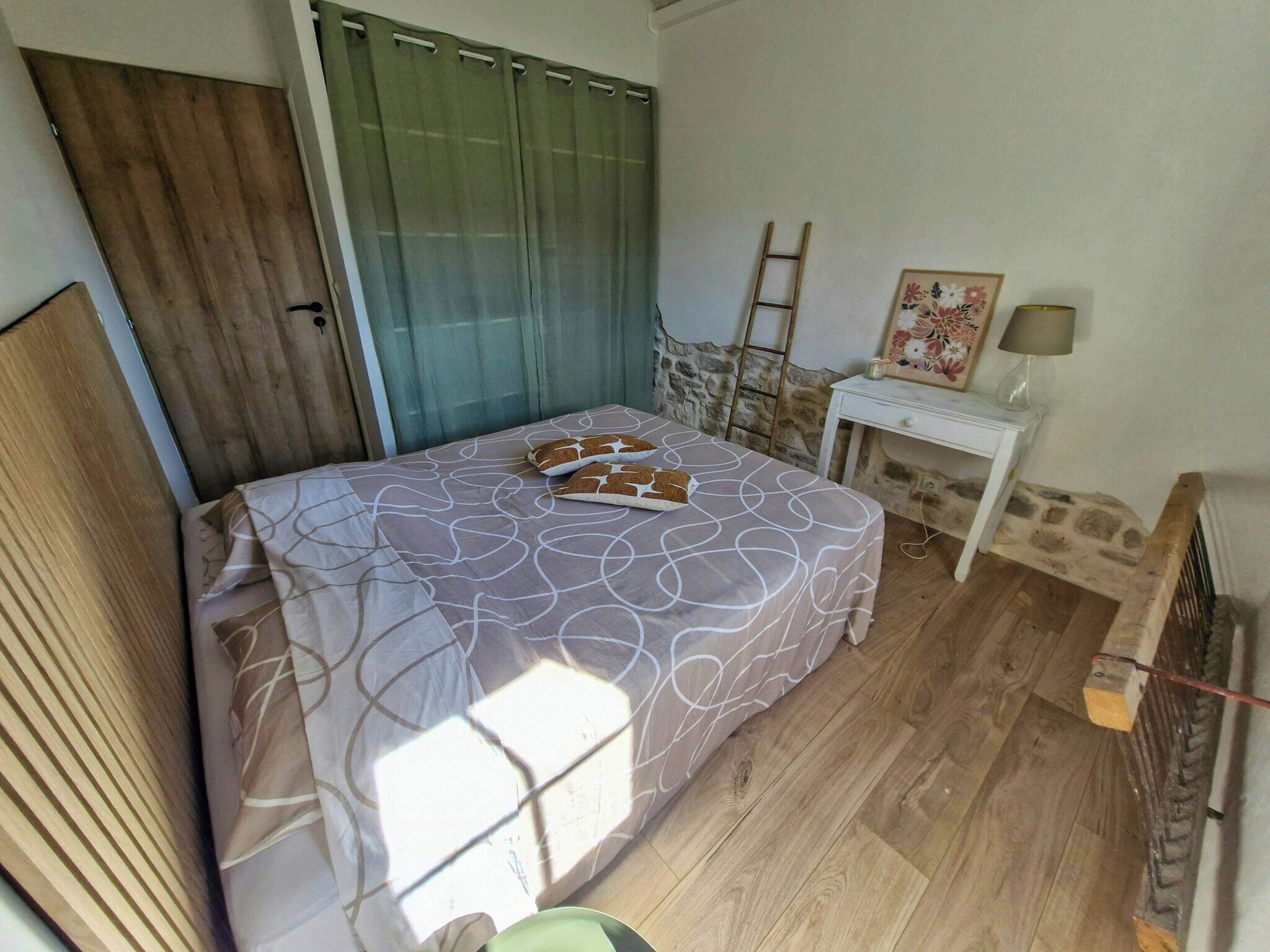 A bedroom with a bed, a nightstand, a ladder, and a window with curtains.