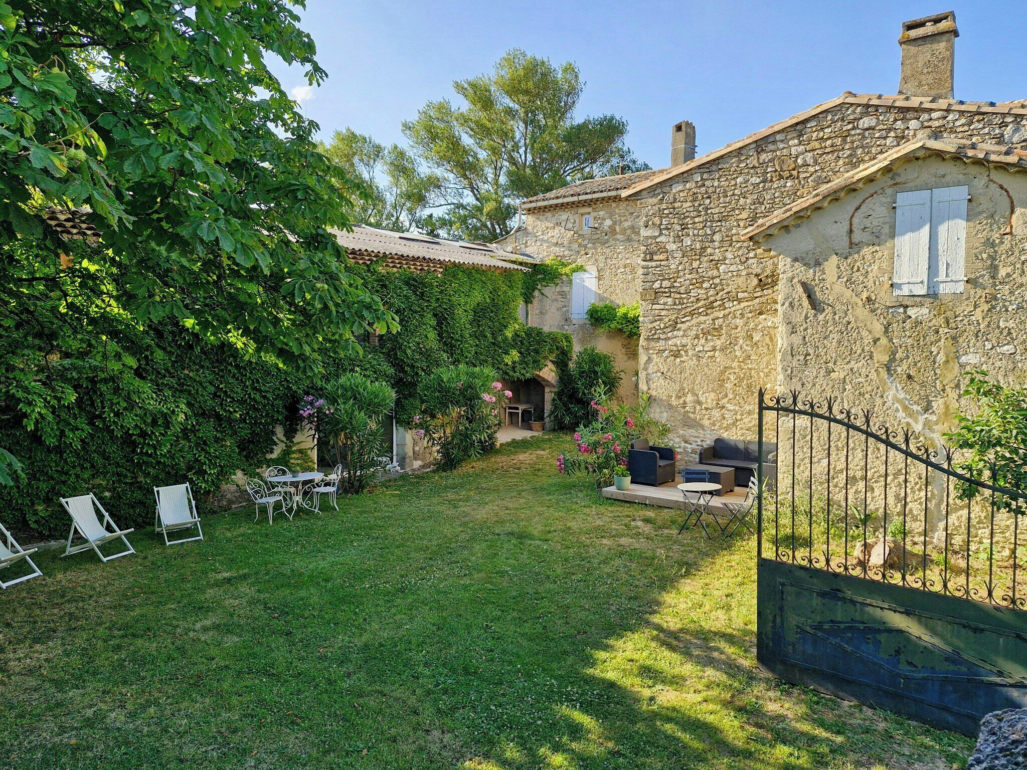 Une maison en pierre avec un jardin, un espace extérieur aménagé pour s’asseoir et un portail en métal.