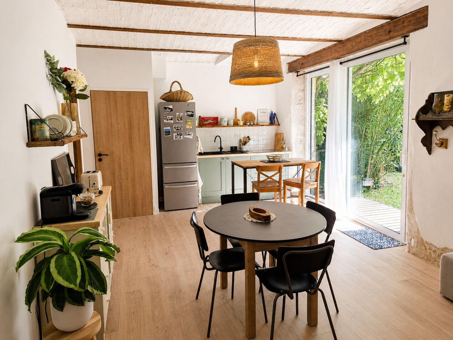 A modern kitchen with a dining area, wooden ceiling beams, and a large window.