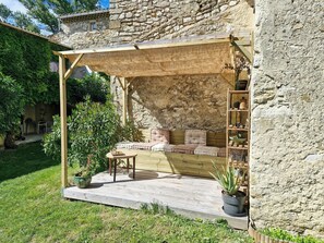 A stone building with a wooden porch, a seating area with cushions, and a small table with a potted plant. - Stone farmhouse near Grignan château in Drôme (Roynac)