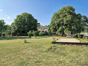 A grassy outdoor area with a stone bench, trees, and a stone building in the background. - Stone farmhouse near Grignan château in Drôme (Roynac)