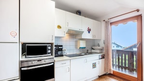 Een keuken met witte kastjes, een magnetron, een oven, een koffiezetapparaat en een raam met uitzicht.