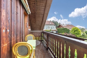 Una terraza de madera con una mesa y sillas, barandilla y vistas a casas y árboles.