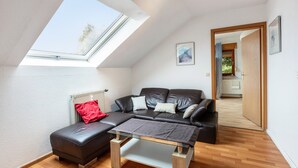 Een moderne loft slaapkamer met dakraam, een leren bank, een glazen salontafel en een houten vloer.
