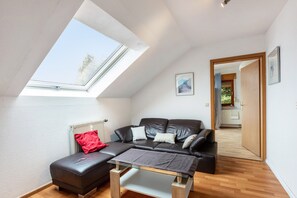 Un dormitorio tipo loft moderno con tragaluces, un sofá de cuero, una mesa de centro de vidrio y suelo de madera.