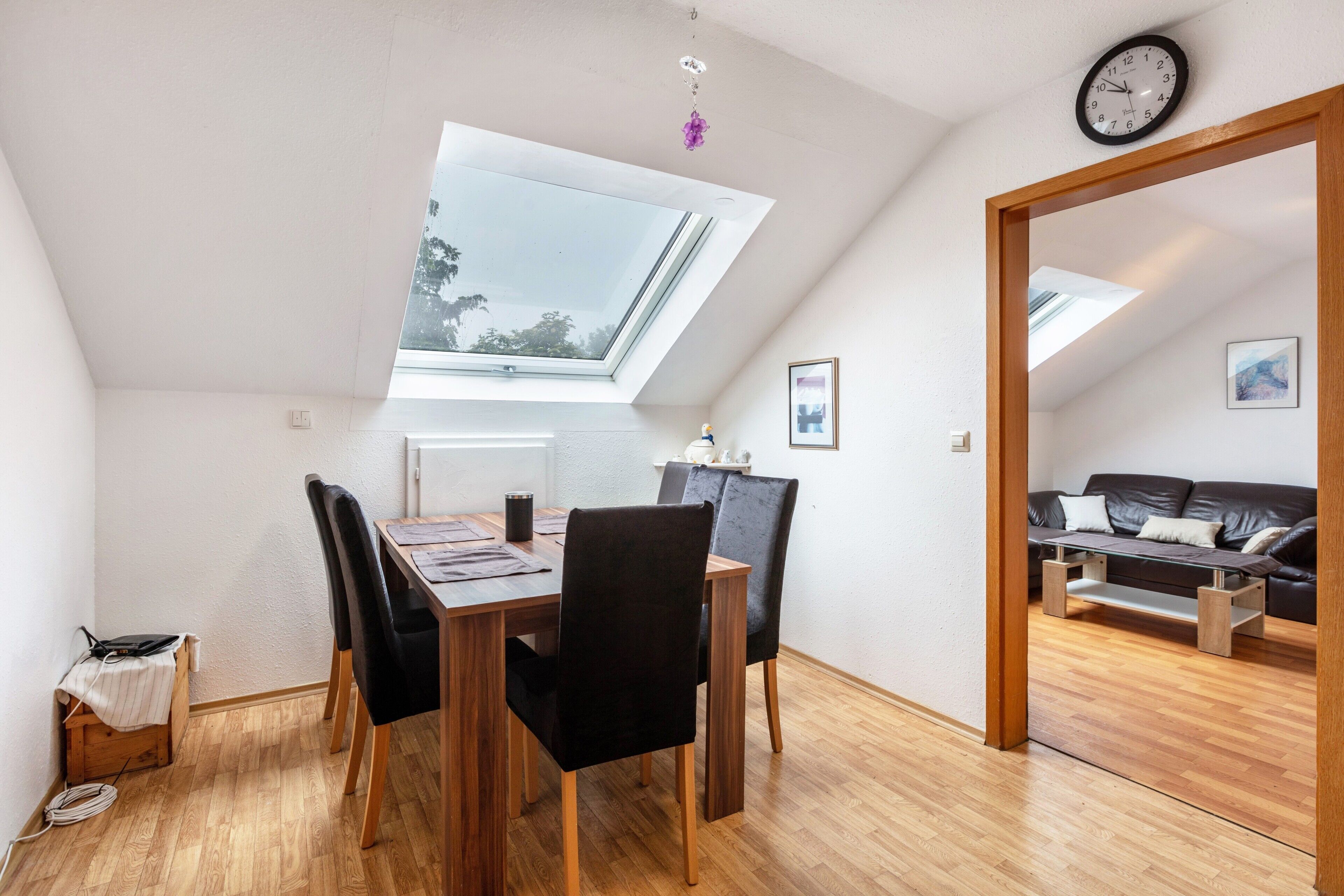 A dining area with a skylight, wooden table, black chairs, and a view of a living room.. Dog-Friendly 4-Room Apartment with Mountain View, Balcony – Near Swiss Border