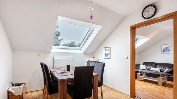 Een eetgedeelte met dakraam, houten tafel, zwarte stoelen en uitzicht op een woonkamer.