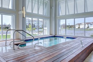Une piscine dotée d’une terrasse en bois, de rampes en métal et de grandes fenêtres donnant sur un quartier résidentiel.