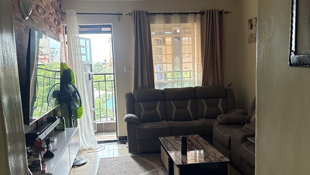 A living room with a sofa, a coffee table, a TV, and a window with curtains. - Bright 2-bedroom apartment with AC in serene Nairobi (Nairobi)