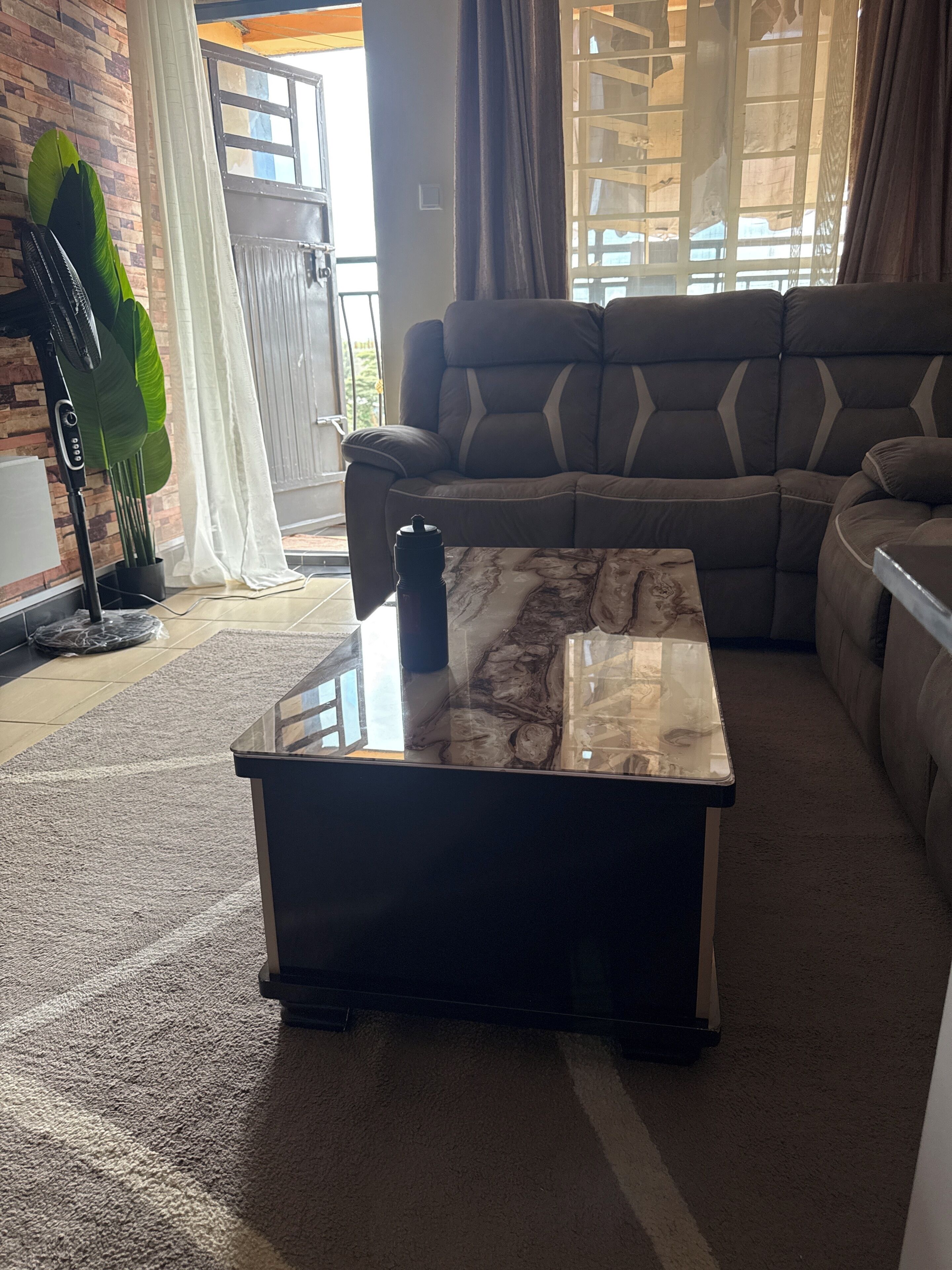 Un salon comprenant un canapé d’angle, une table basse en verre et une grande fenêtre avec des rideaux.