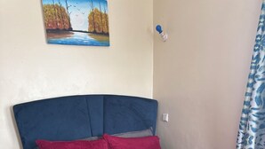 A bed with a blue headboard, red and grey bedding, and a painting of a landscape on the wall. - Bright 2-bedroom apartment with AC in serene Nairobi (Nairobi)