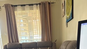 A sectional sofa with a built-in coffee table, a flat-screen TV, and a window with curtains. - Bright 2-bedroom apartment with AC in serene Nairobi (Nairobi)