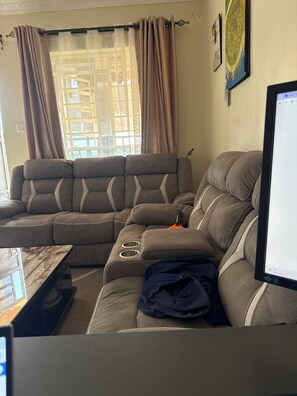 Ein modulares Sofa mit integriertem Couchtisch, einem Flachbildfernseher und einem Fenster mit Vorhängen.