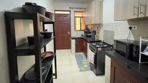 A compact kitchen with a gas stove, a microwave, and a sink. There is a door leading to another room. - JB VACATION HOME (Mombasa)