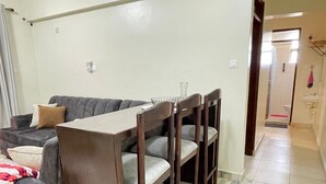 A dining area with a table and chairs, a sofa, and a bathroom visible in the background. - JB VACATION HOME (Mombasa)