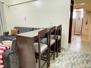 A dining area with a table and chairs, a sofa, and a bathroom visible in the background. - JB VACATION HOME (Mombasa)