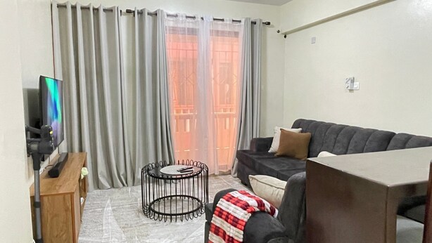 A living room with a sofa, a TV, a coffee table, and a window with curtains. - JB VACATION HOME (Mombasa)