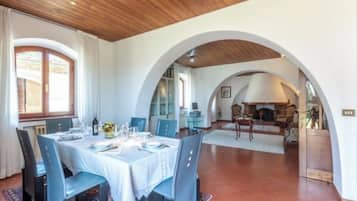 Zona pranzo con tavolo imbandito per quattro, una porta ad arco e una cucina visibile attraverso l'arco.