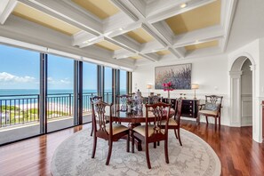 A dining area with a view of the ocean, large windows, and a chandelier. - 🐬Top Floor🌞Incredible Water Views🌴Huge Private Balcony🐠Beachfront Community (Treasure Island)