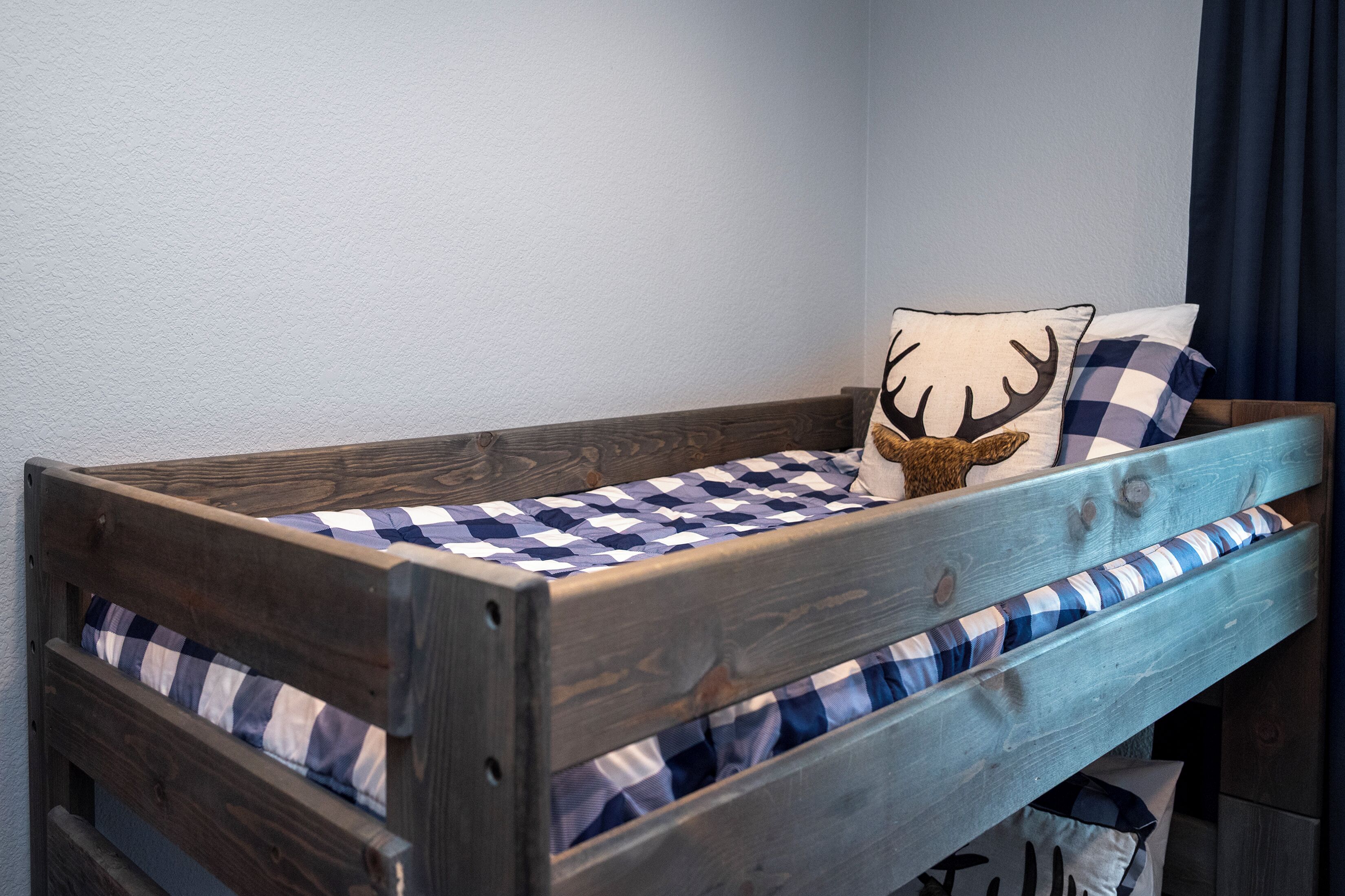 Una cama litera de madera con ropa de cama a cuadros, un cojín con un diseño de ciervo y una cortina oscura.