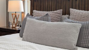 Una cama con cabecera acolchada, una lámpara de noche y una mesita de madera con lámpara.
