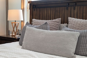 Uma cama com cabeceira acolchoada, luminária de cabeceira e mesa de cabeceira de madeira com uma luminária.