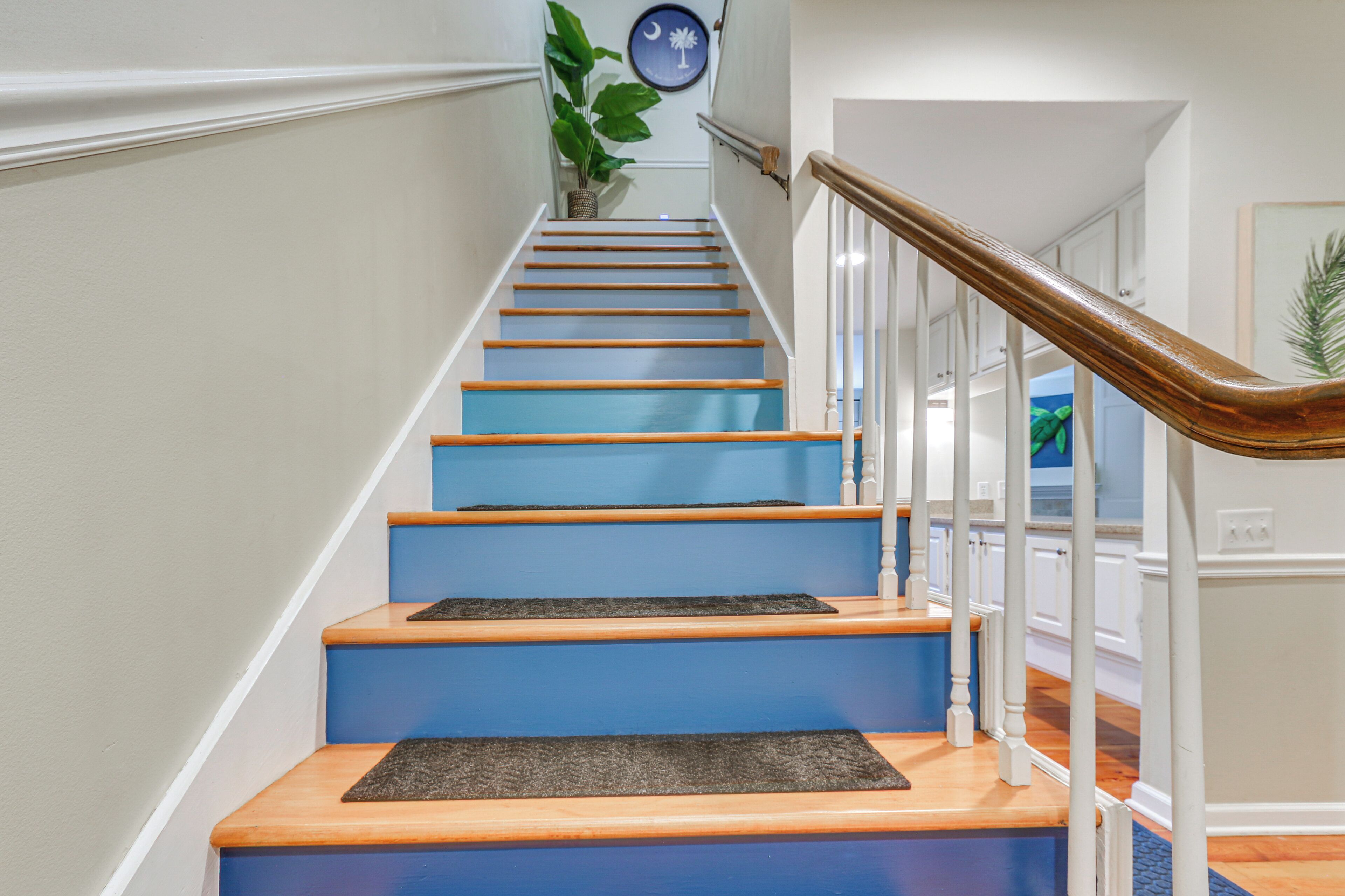Eine Treppe mit blauen Stufen und Holzhandläufen, die zu einer Zwischenebene mit einer Pflanze und Wandkunst führt.