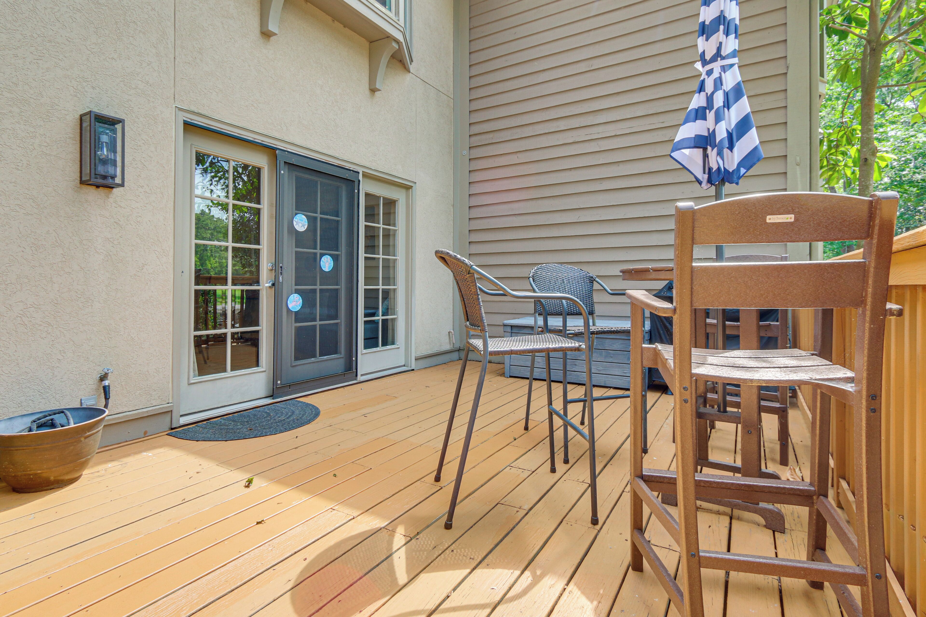 A wooden deck with outdoor furniture, a sliding glass door, and a blue and white striped umbrella.