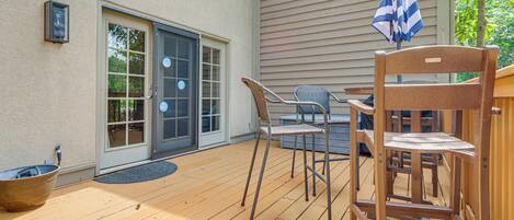 A wooden deck with outdoor furniture, a sliding glass door, and a blue and white striped umbrella.