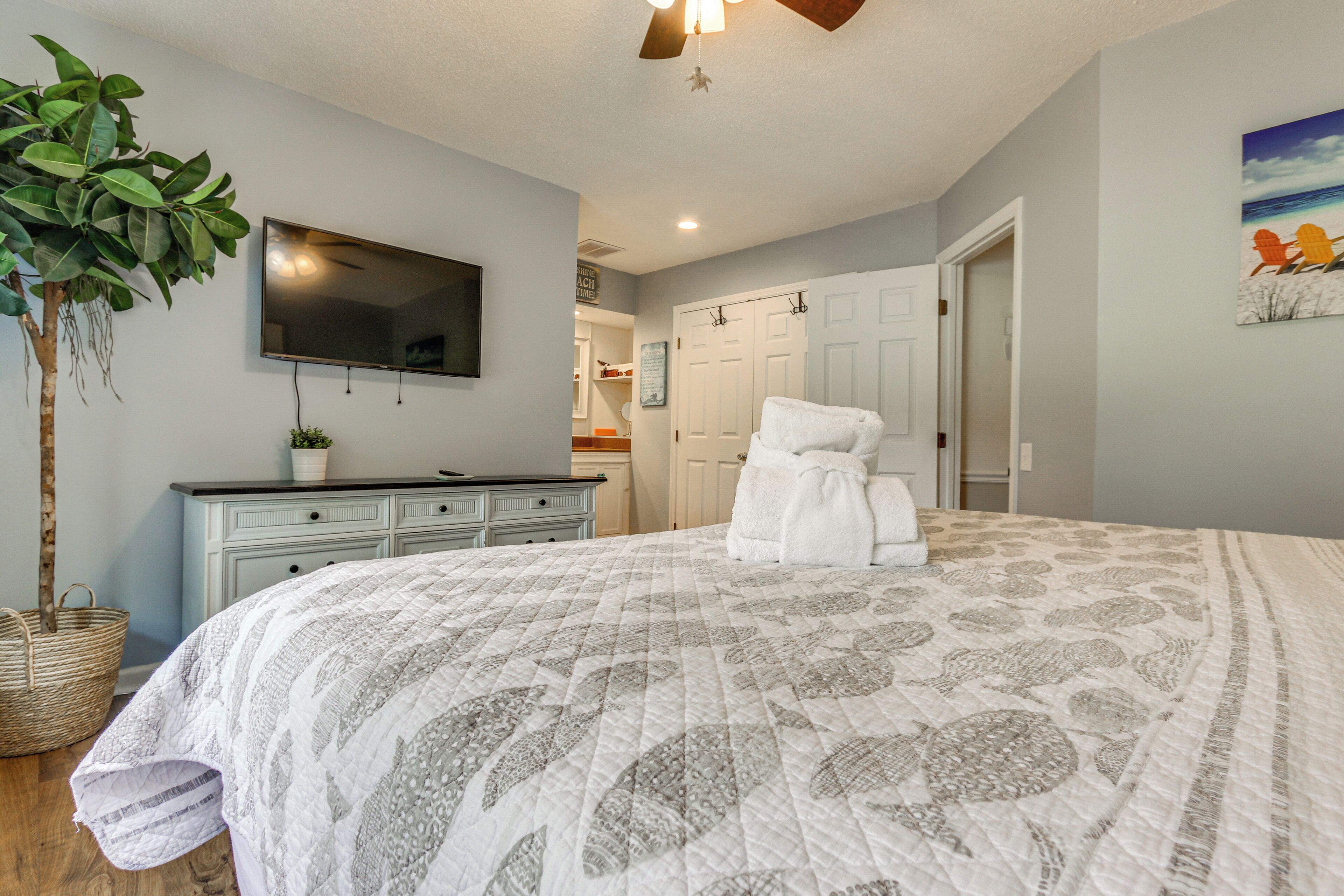 A bedroom with a bed, a television, a plant, and a door leading to a bathroom.