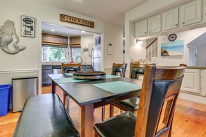 Ein Essbereich mit Holztisch und Stühlen, im Hintergrund eine Küche und ein Schild mit der Aufschrift 'BEACH HOUSE'.