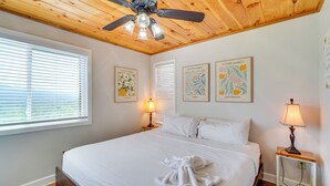 A bedroom with a wooden ceiling, a bed with white linens, two bedside lamps, and framed pictures on the wall. - Whispering Woods: Smoky Mountain Resort Escape (Gatlinburg)