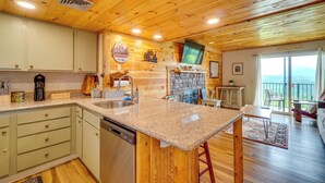 A kitchen with granite countertops, wooden cabinets, a dishwasher, and a stone fireplace. - Whispering Woods: Smoky Mountain Resort Escape (Gatlinburg)